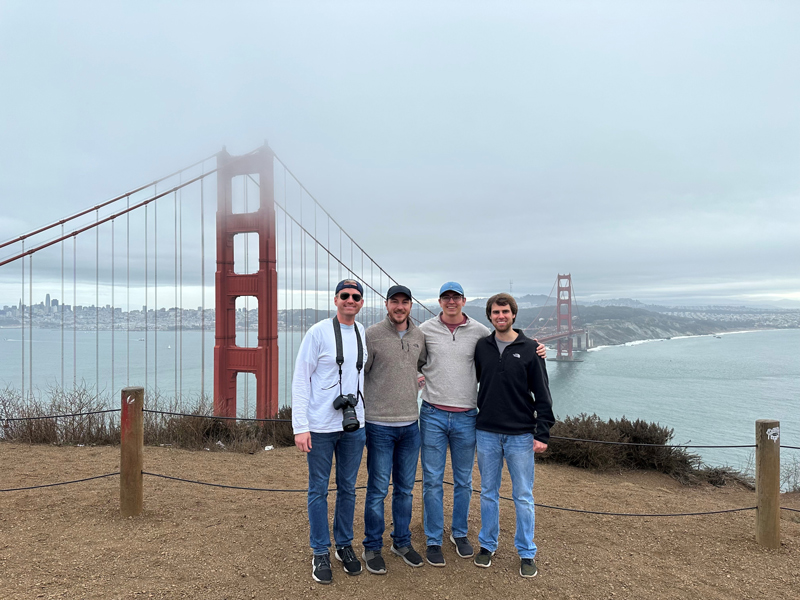 Four people stand in front of the fog-covered Golden Gate Bridge in San Francisco.